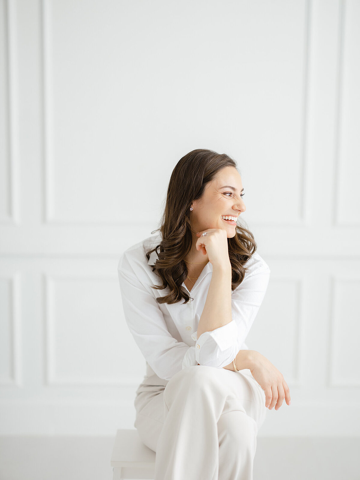 A casual branding headshot of a DFW small business owner sitting on a stool as she looks out of the window laughing.