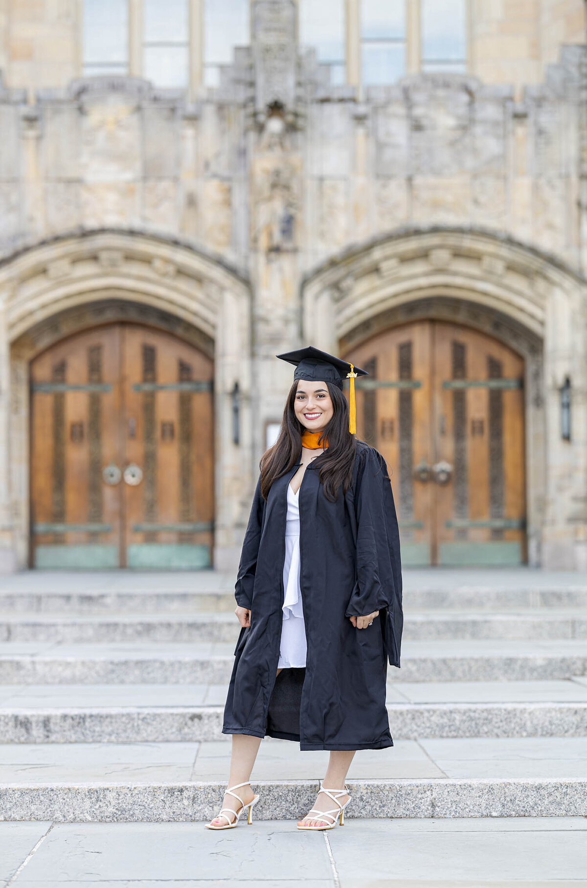 Graduate girl wearing a cap and gown smiling during her graduate photo session at the Sterling Library on Yale University campus in Connecticut