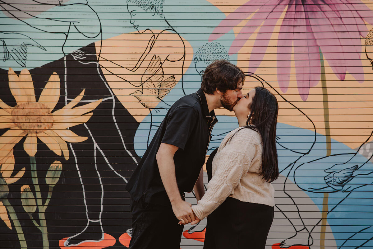 A couple holding hands and kissing in front of a mural 