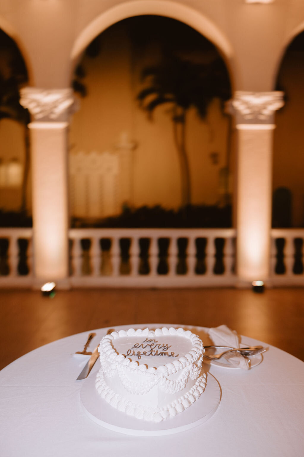 Heart shape vintage wedding cake on ivory tablecloth under arches with an orange glow