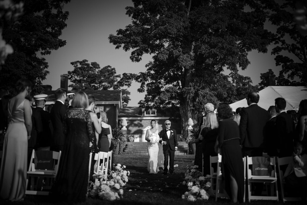 A bride walks down the aisle with her father at an outdoor ceremony at a destination wedding in Vermont