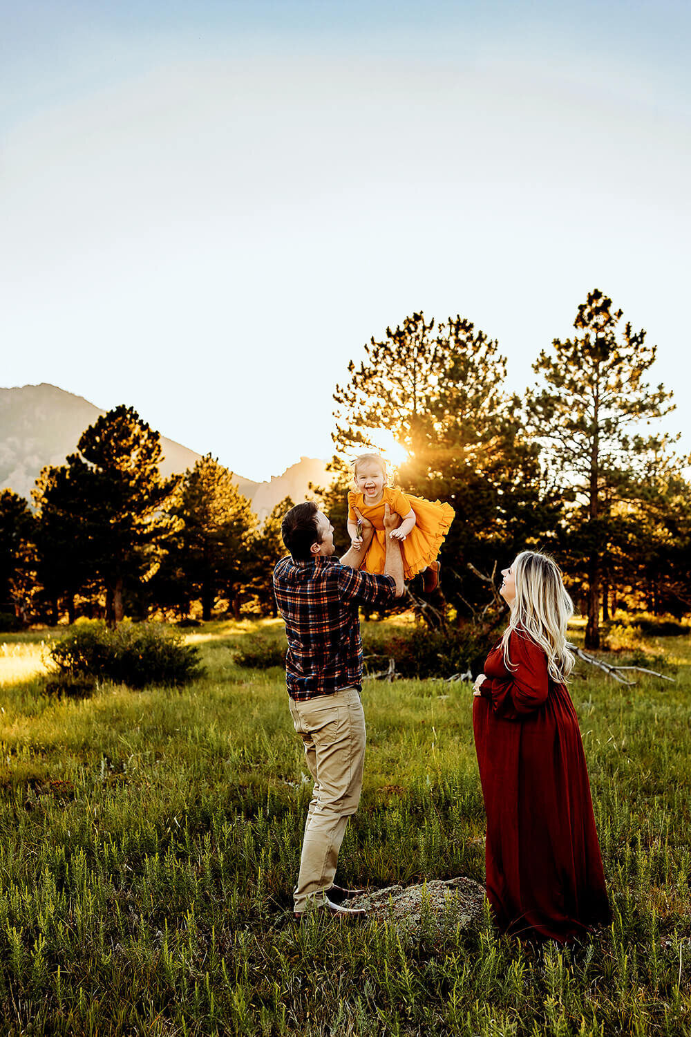 Pregnant mom and dad playing with toddler daughter in the mountain sunset of Boulder.