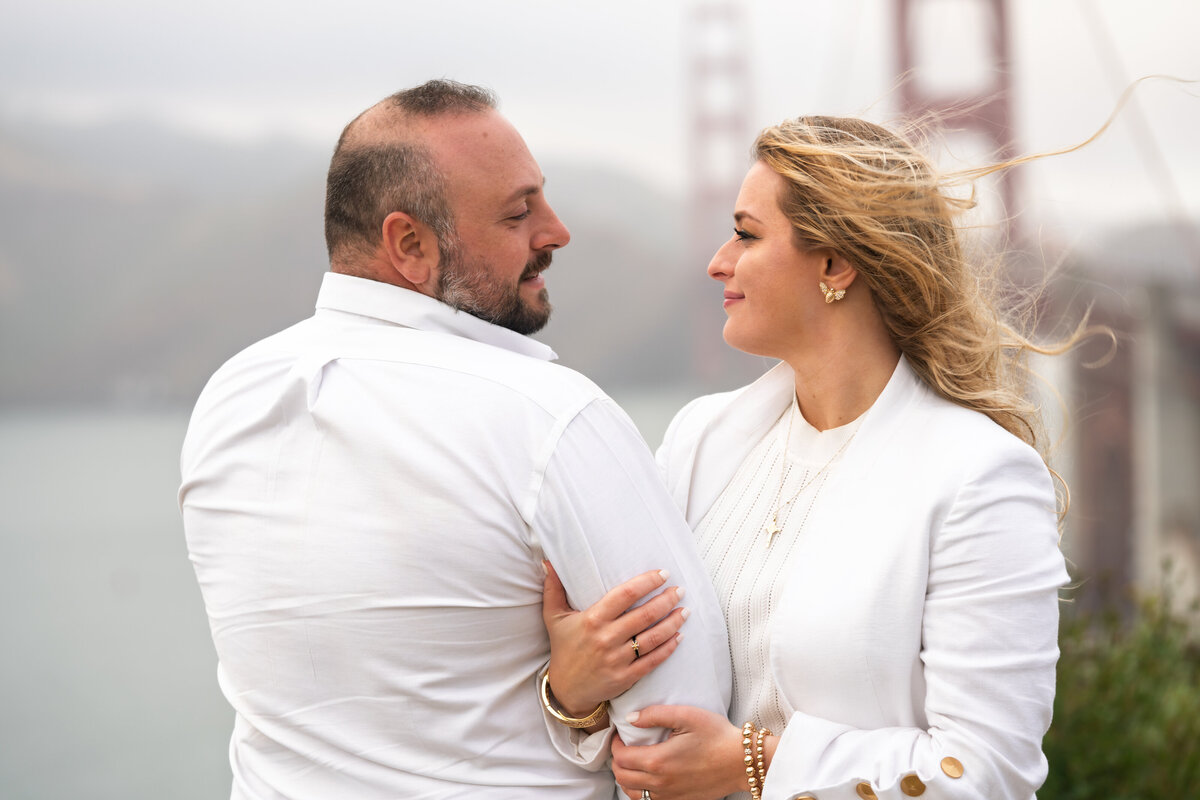 Couple embracing and looking at each other while posing in front of the golden gate bridge
