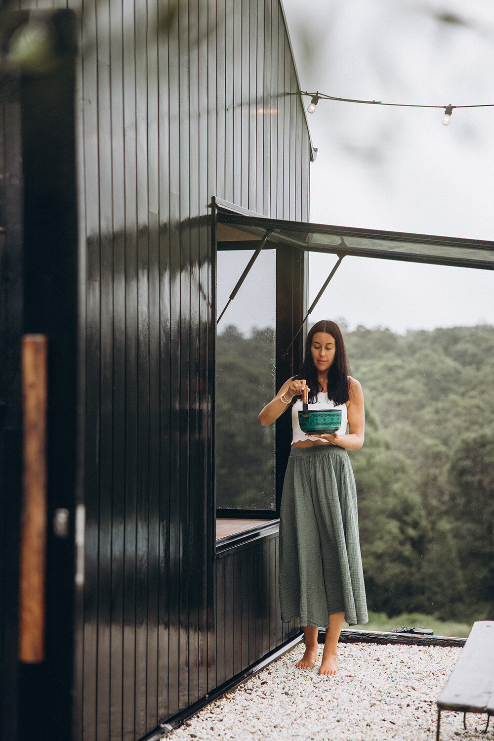 Sunshine Coast branding photographer captures a scenic, editorial branding portrait of a woman standing at a black cabin in the hills.