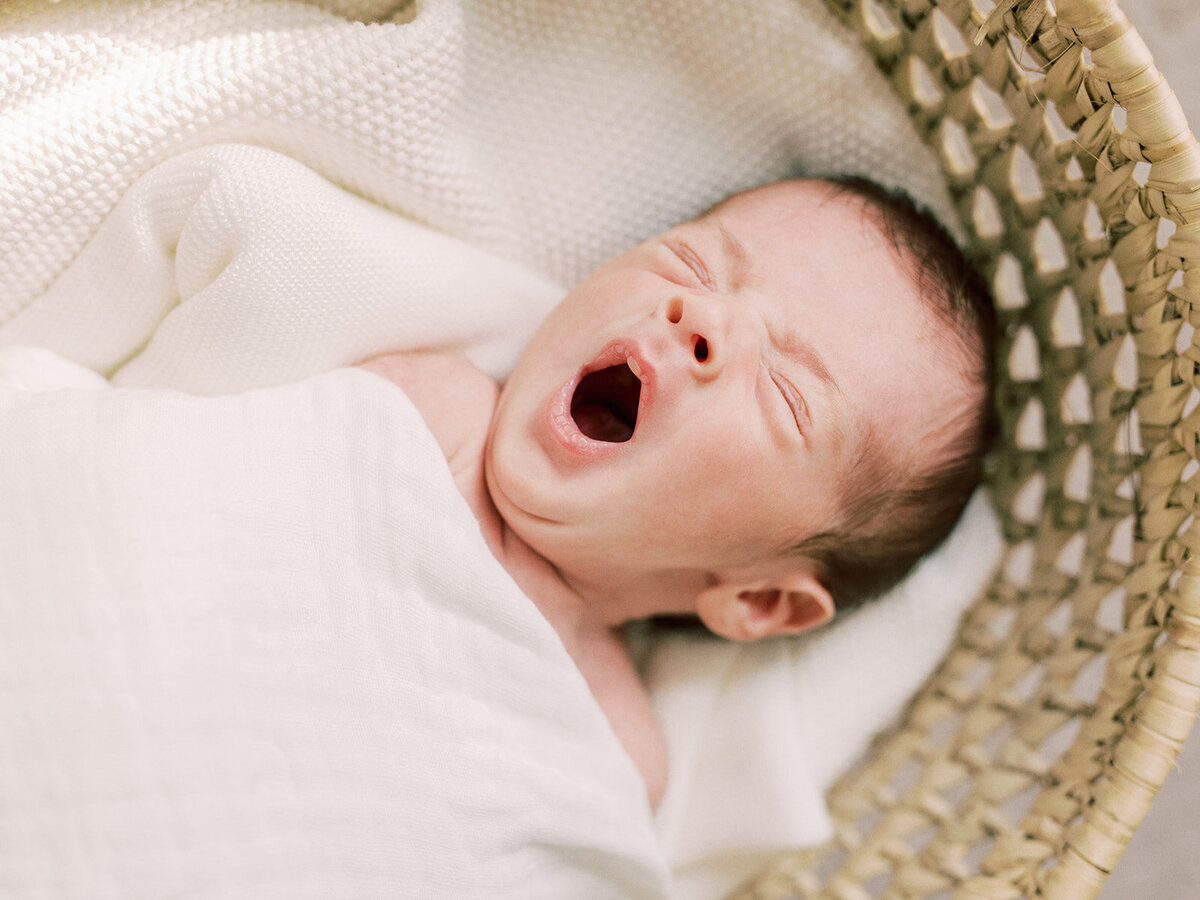 A newborn yawning while laying in a basket during a newborn photography session in Richmond by Katie Stansfield Photography.