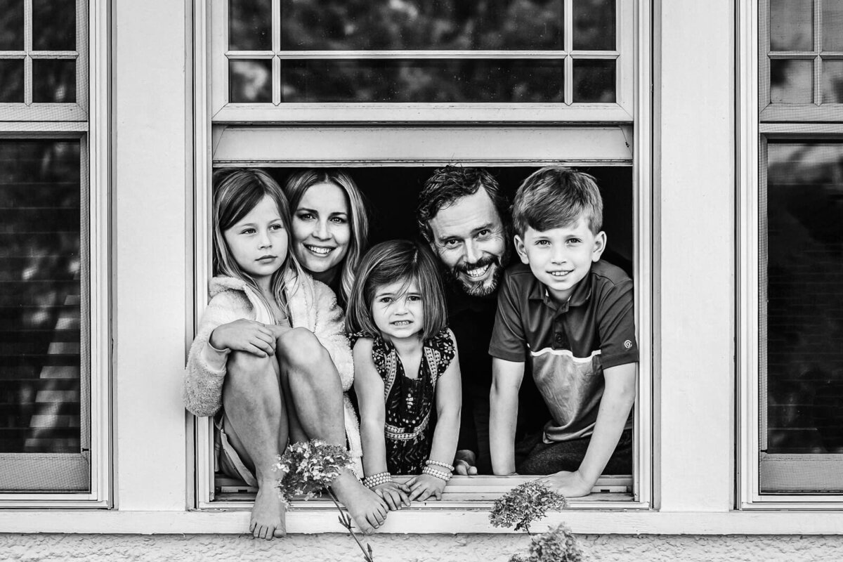 A black and white image of a family with three small children looking out a window of their home during a photography session with Minneapolis family photographer, Kate Simpson.