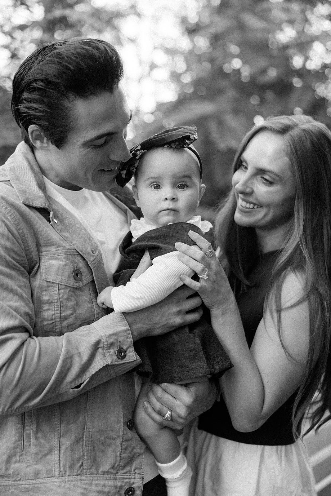 Family of three hugs each other and smiles at their little baby. 