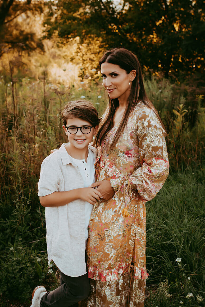 a mother and son standing side by side in a pretty field at sunset