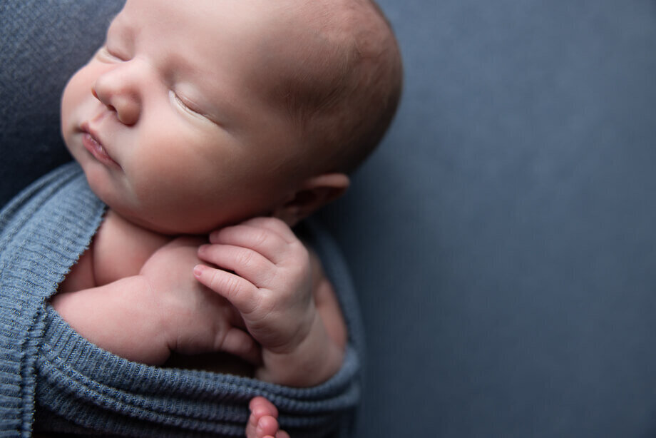 close up detail shot of a newborn boys hands.  The baby is swaddled with his hands and toes peeking out.