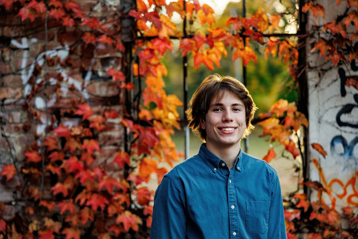 Orange leaves and an old window are behind this Cleveland senior portrait subject.