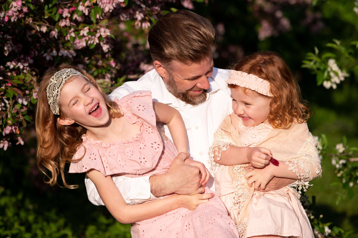family photography in Ottawa of a dad tickling his two little girls with red hair and pink dresses