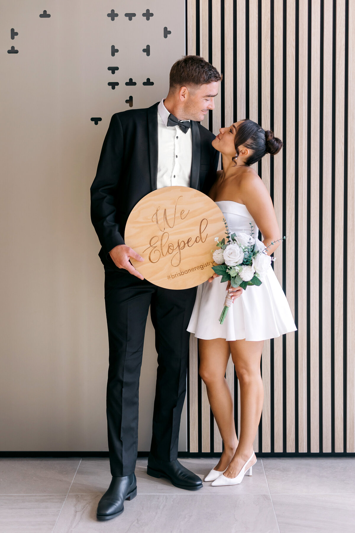 Brisbane wedding couple eloping at the Registry Office, holding a 'We Eloped' sign and bouquet – captured by Brisbane wedding photographer Leanne James.