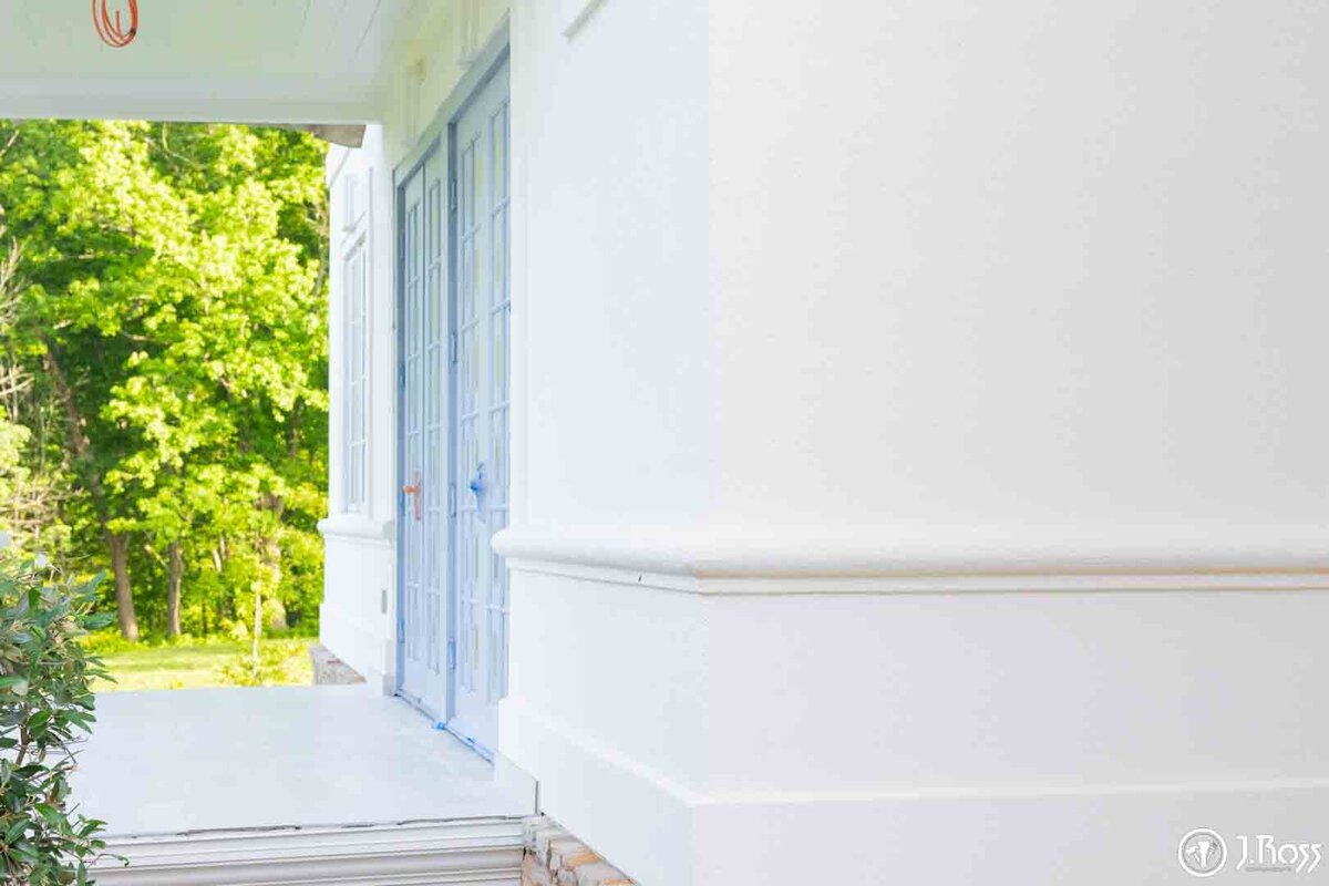 Extreme close-up of the clean, sharp lines of the base and molding on the white stucco wall next to a blue-taped French door, showing flawless trim home exterior painting Bristol, VA.
