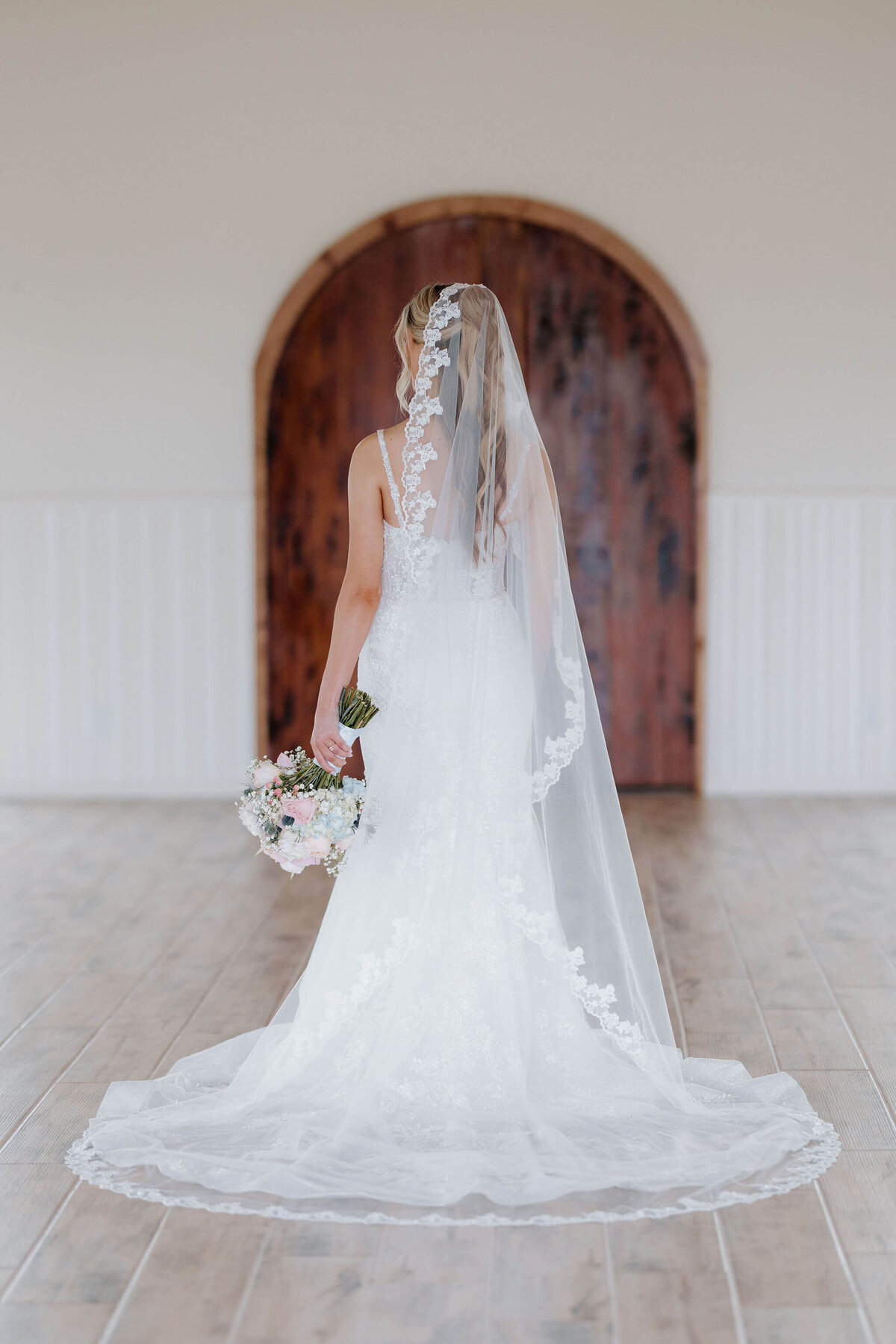 Bridal portratis in long white lace wedding gown, cathedral length lace veil, and summer inspired wedding bouquet