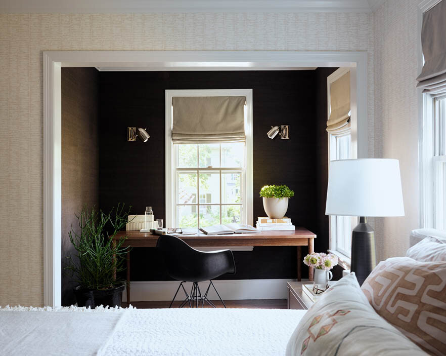 Discover the nook off the primary bedroom in a historic Hingham home, featuring black grasscloth wallpaper, an oversized desk, Ralph Lauren sconces, and a perfect spot for reading or working from home.