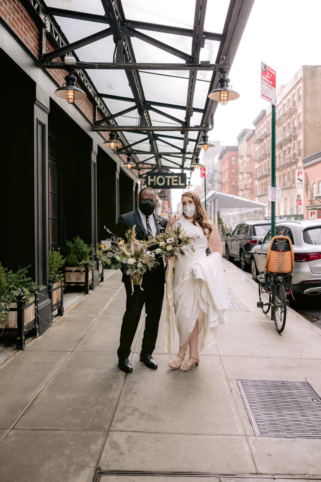 The bride and the groom are holding flower bouquets outside of Ludlow Hotel.