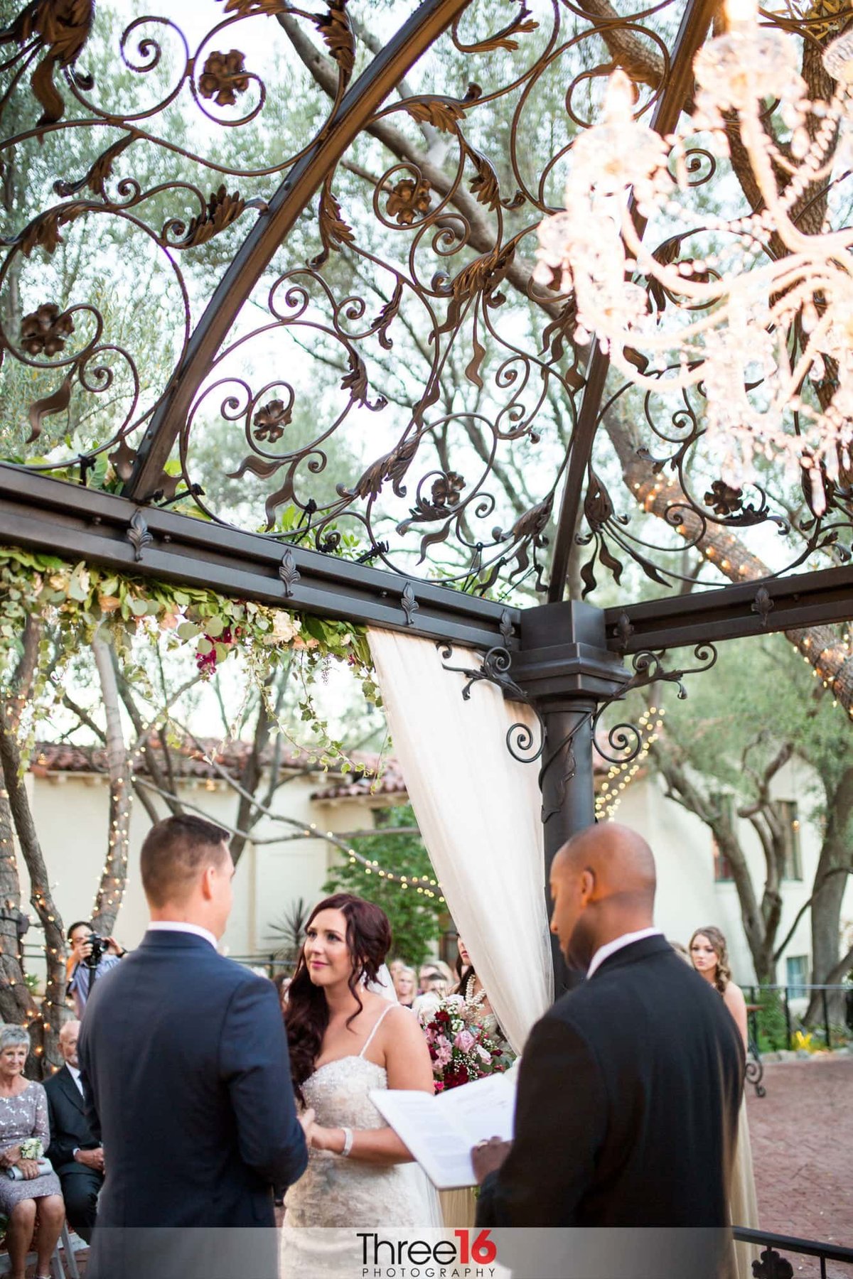 Bride and Groom face each other and hold hands under a gazebo as the officiant reads the vows at the Padua Hills theater