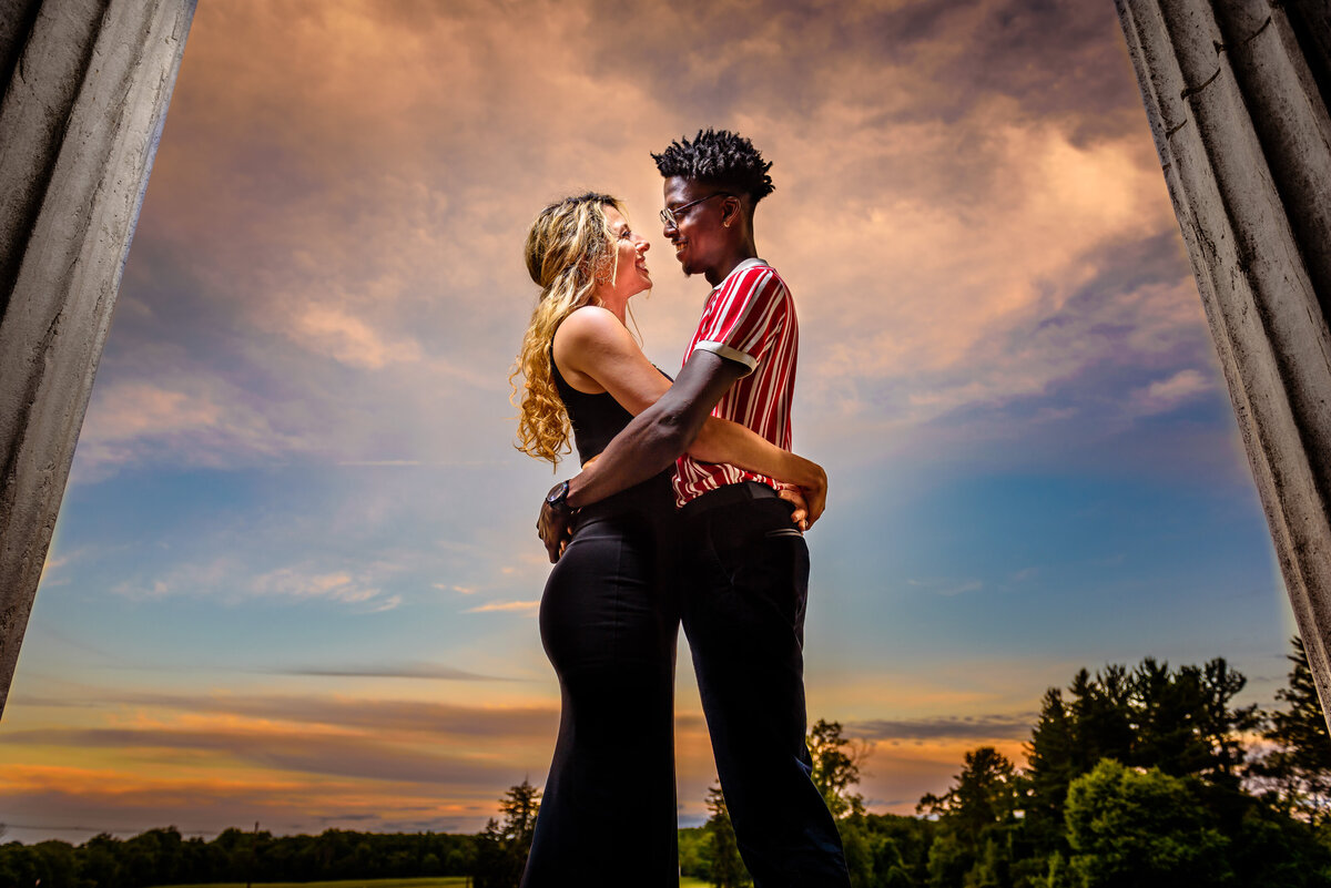 A biracial couple embraces with a beautiful sunset backdrop behind them