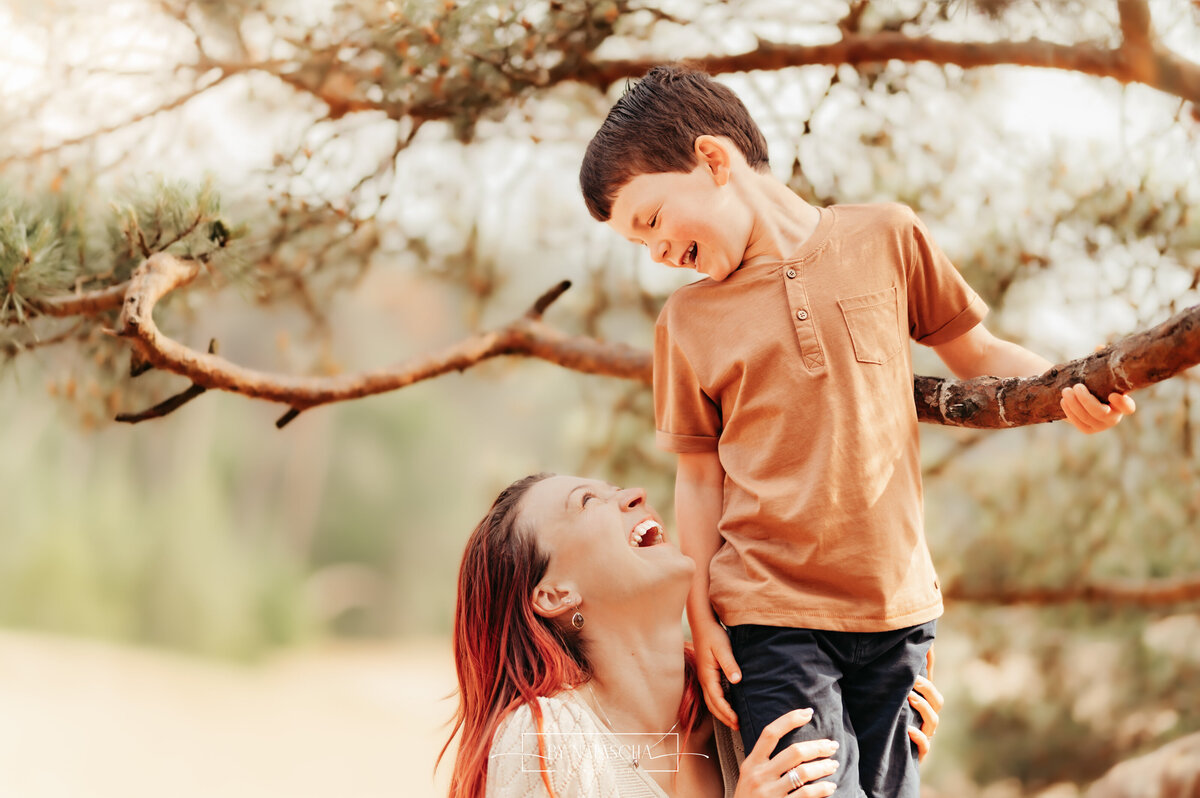 Mama en zoon lachend naar elkaar in Drunense Duinen bij een boomtak
