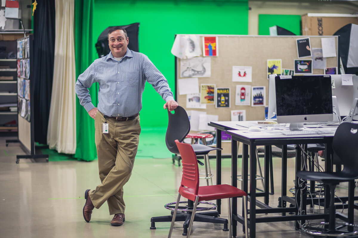 Male graphic designer teacher standing at a desk in his classroom in front of a green screen