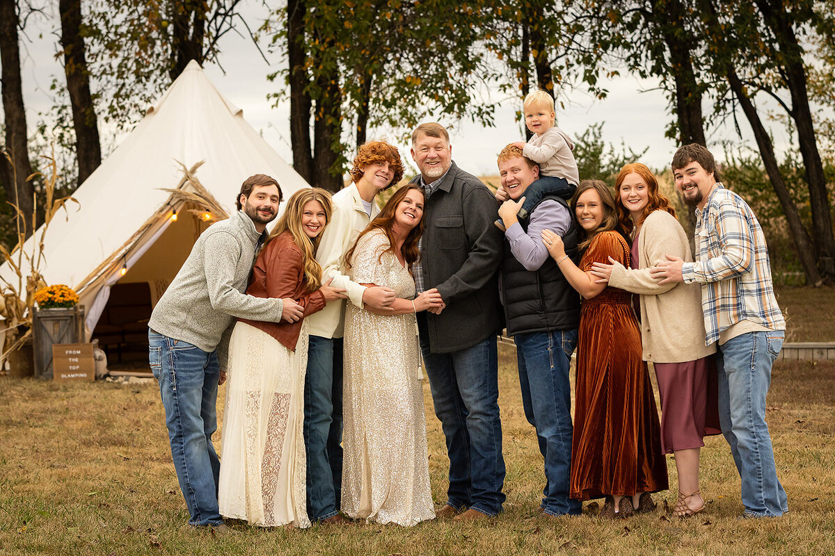 extended family with yurt in background and baby on shoulders