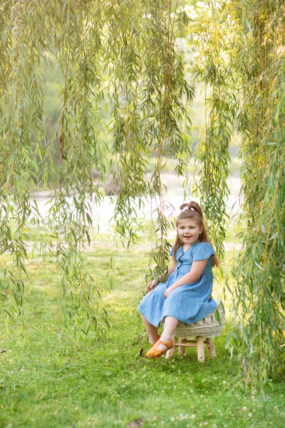 preschooler sits on stool under a willow tree at Waterworks Park
