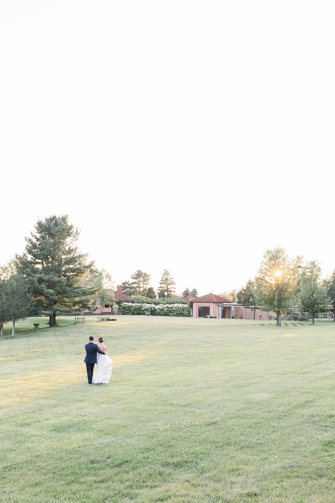 Newlyweds share a quiet intimate moment in a large lawn watching the sunset