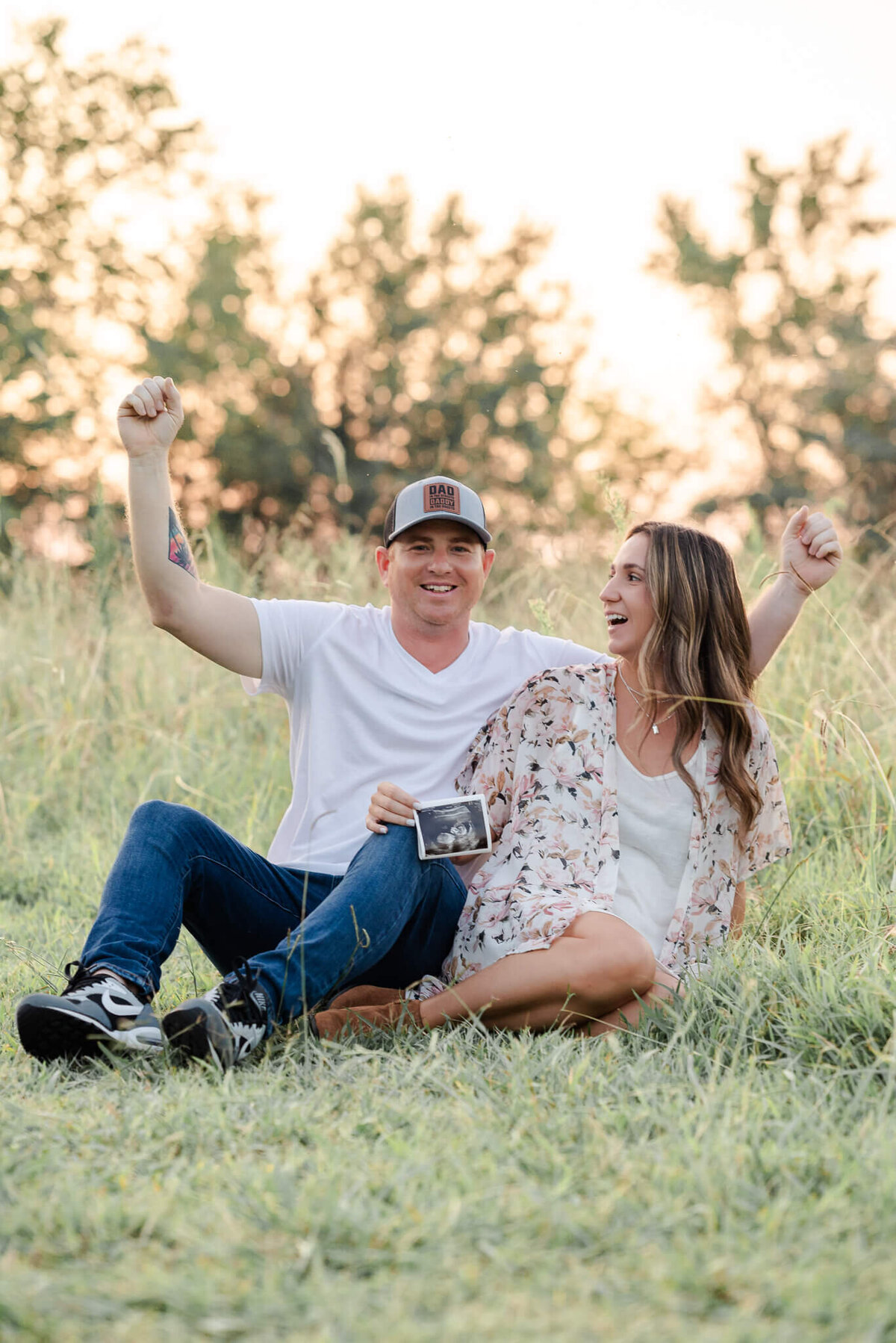 A father-to-be pumps his arms in excitement while his partner holds up their sonogram in their pregnancy announcement photo.
