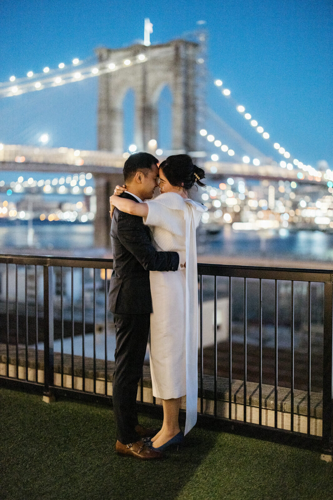Side view of the bride and the groom staring at each other hugging, heads touching with the Brooklyn Bridge in the background