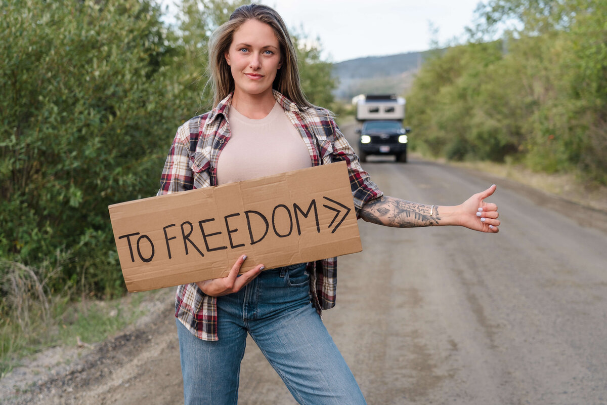 woman holding freedom sign in front of truck hitching a ride for creative brand shoot