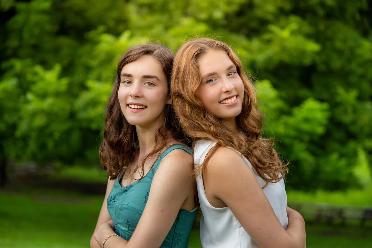 sisters posing back to back for the camera with a vineyard in the background