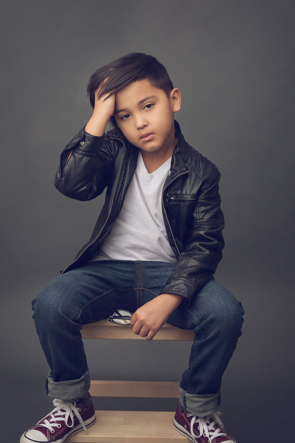 Young boy sitting on a stool, hand in hair, facing the camera. Houston, TX.