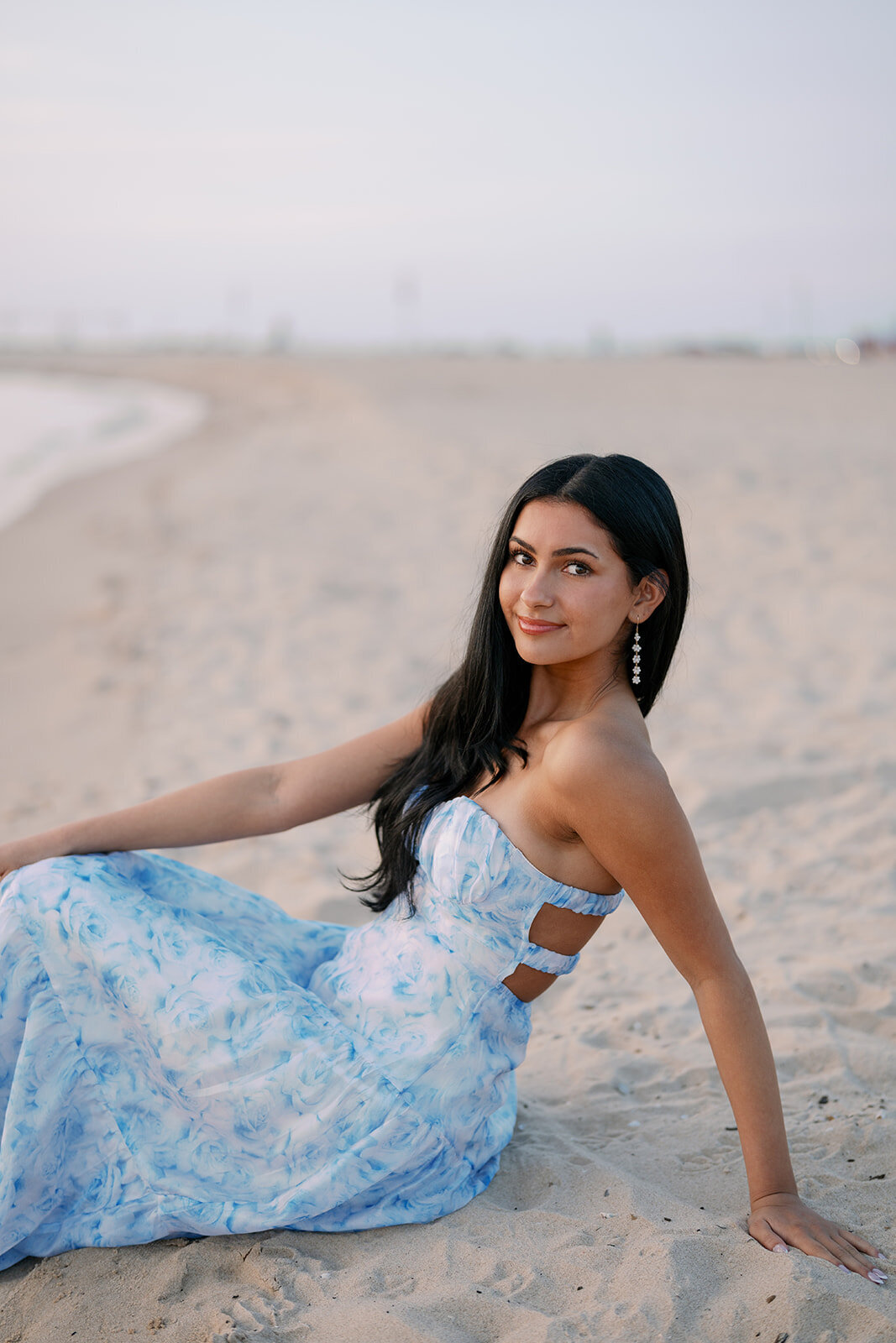 Senior girl sitting in the sand at South Haven North Beach during her sunset senior photo session.