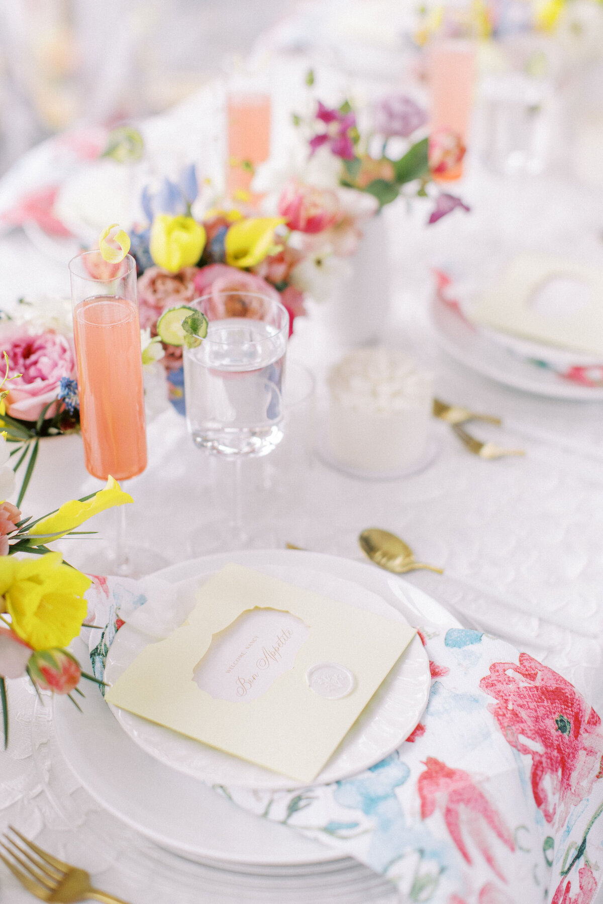 A beautifully set table with floral arrangements, champagne flutes, and a handwritten note on a plate. There are colorful flowers and patterned napkins enhancing the elegant dining setup—perfect for weddings in Banff, Alberta.