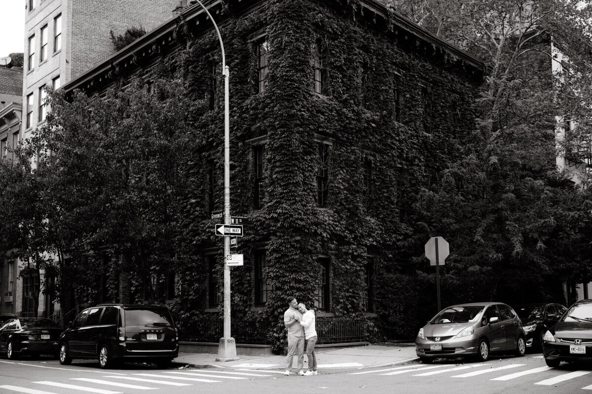 Black and white photo of the engaged couple standing in the corner of an ivy-covered building at West Village, NYC. Image by Jenny Fu Studio