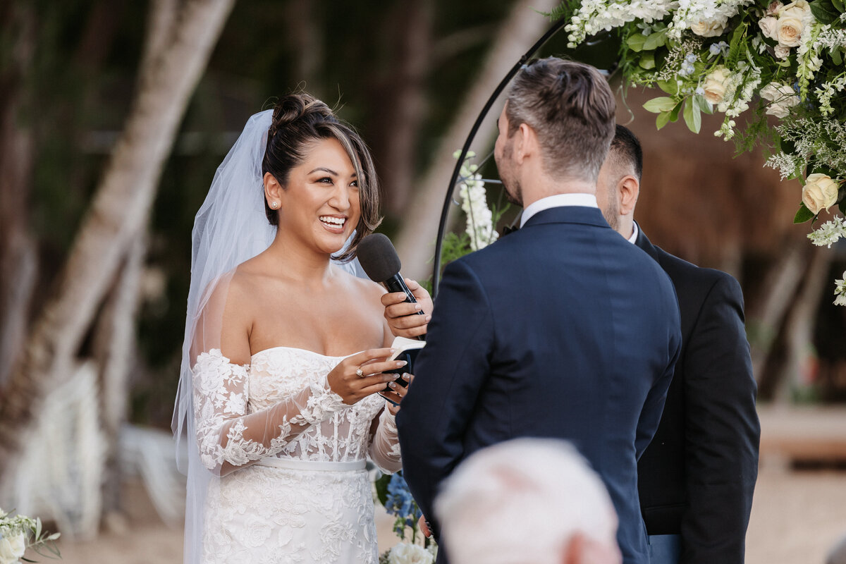 Bride with microphone in front of her reading vows smiling looking at groom