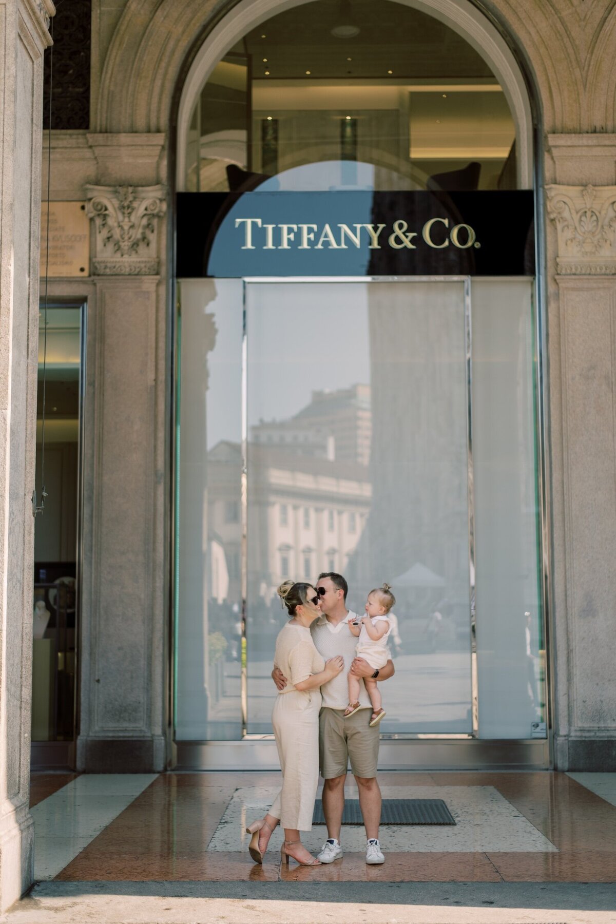 Stylish couple posed with their child outside Tiffany & Co., evoking timeless elegance
