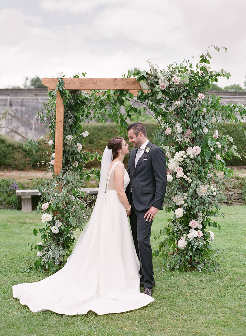 Ireland & US Wedding Planner, bride and groom kissing under greenery wrapped arch