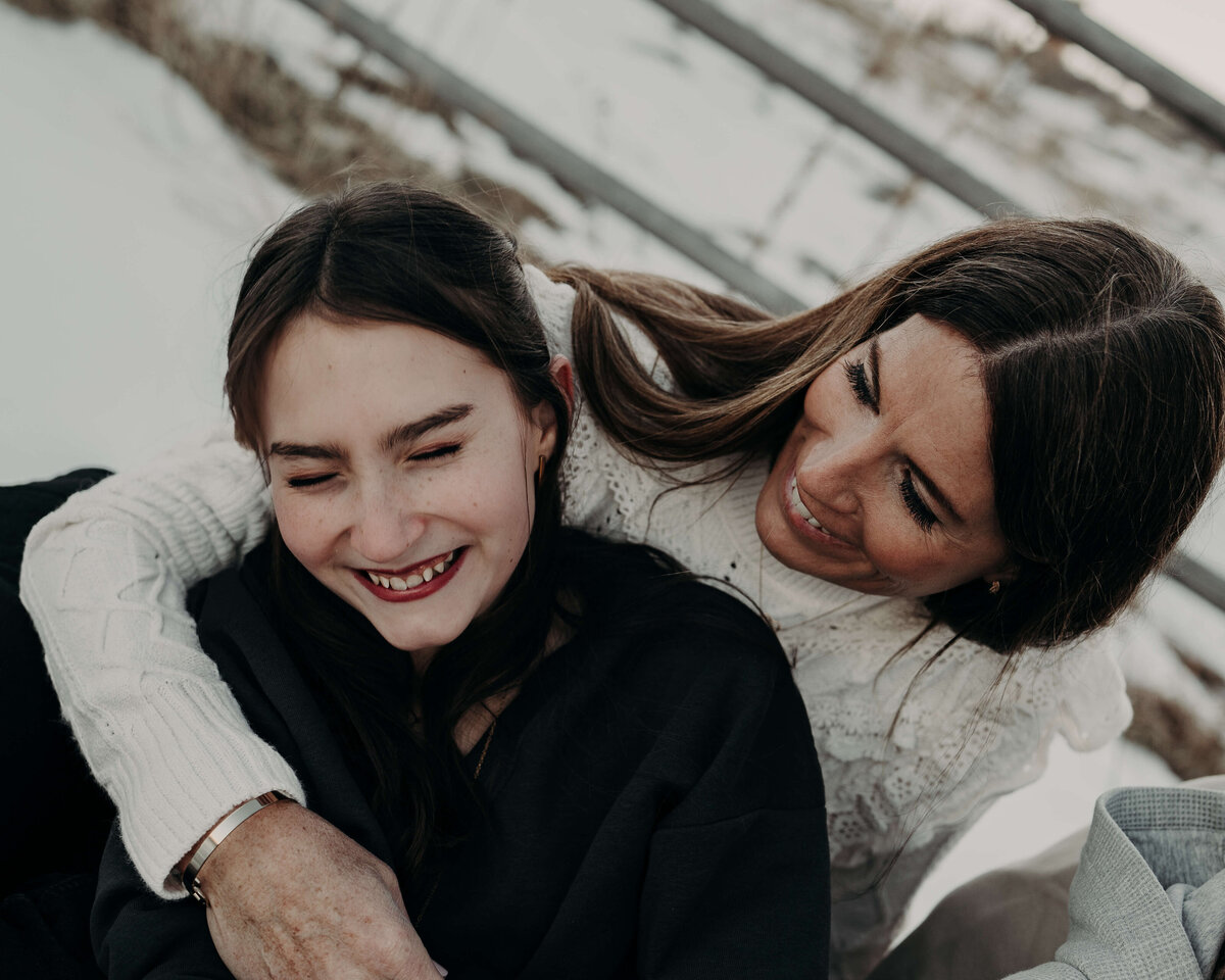 A mother and daughter burst out laughing while cuddling during an outdoor photography session in Denver, Colorado.