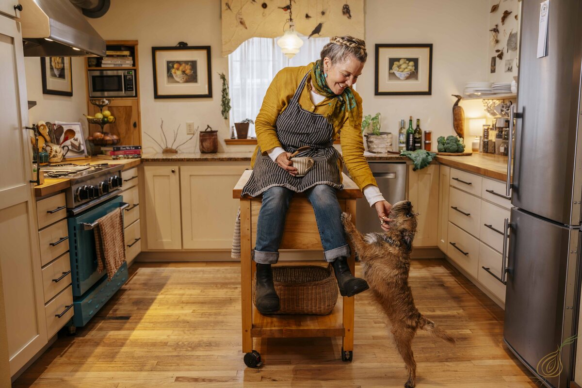 A woman sits on a kitchen island, smiling at her dog, creating a warm and inviting home atmosphere.