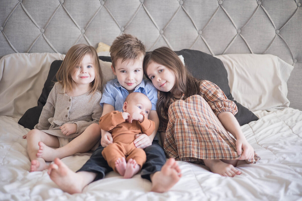 Young siblings, two boys, two girls sitting on a bed