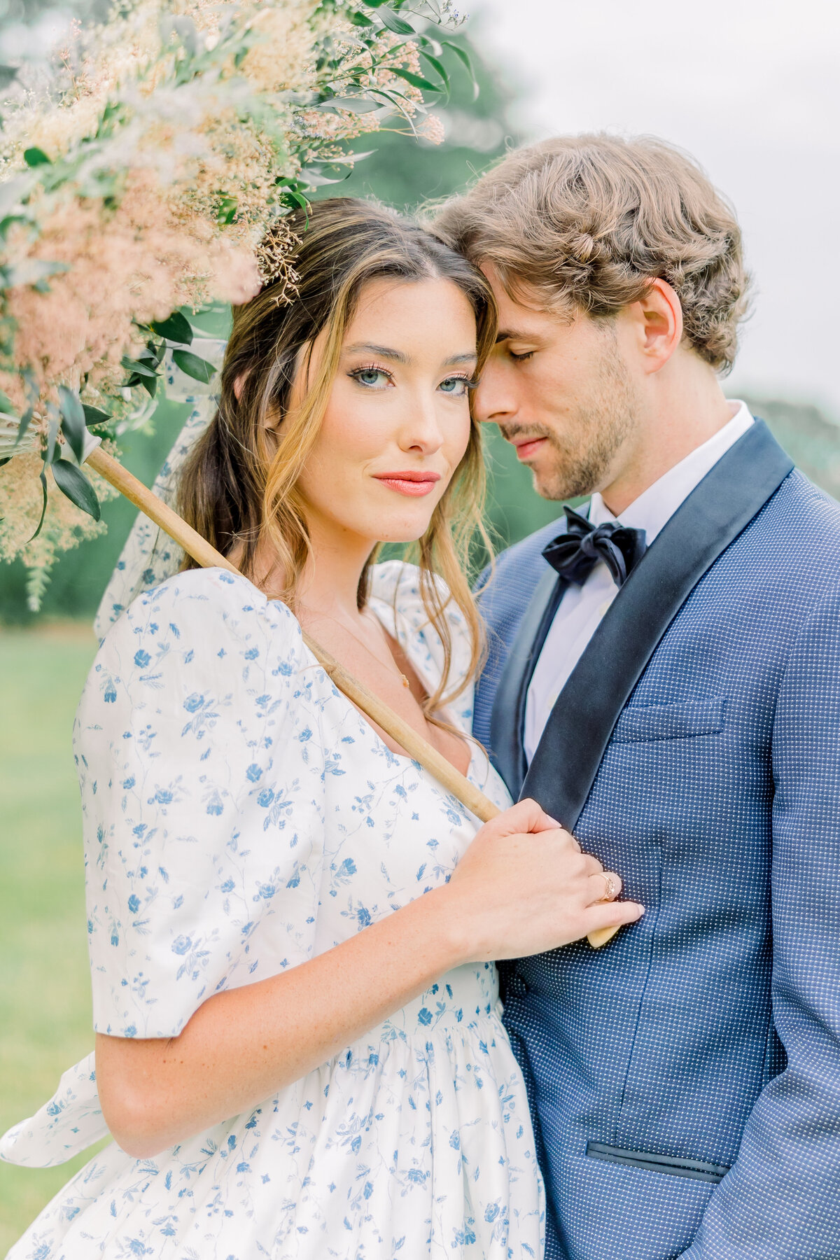 Groom nuzzling bride during portraits while she holds a floral parasol