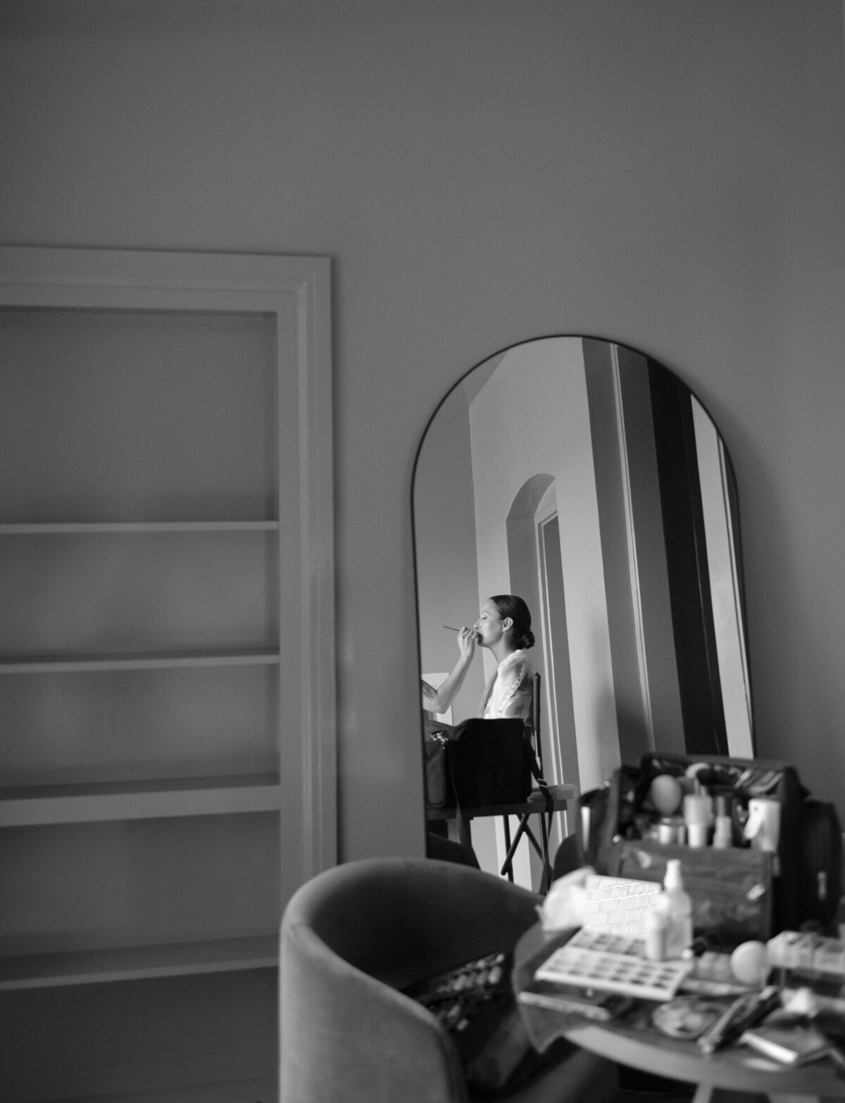 reflected in a mirror with a table full of makeup in the foreground, a bride has her wedding makeup done in a unique Detroit venue, 1 room hotel
