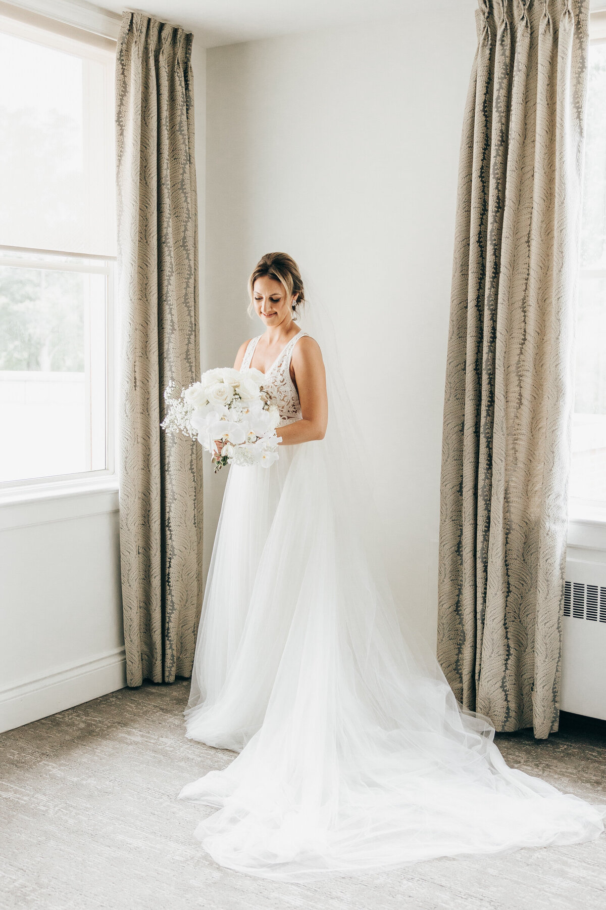 A full length photo of a  stunning bride holding her gorgeous, cascading, white wedding bouquet with white orchids, baby's breath and white roses