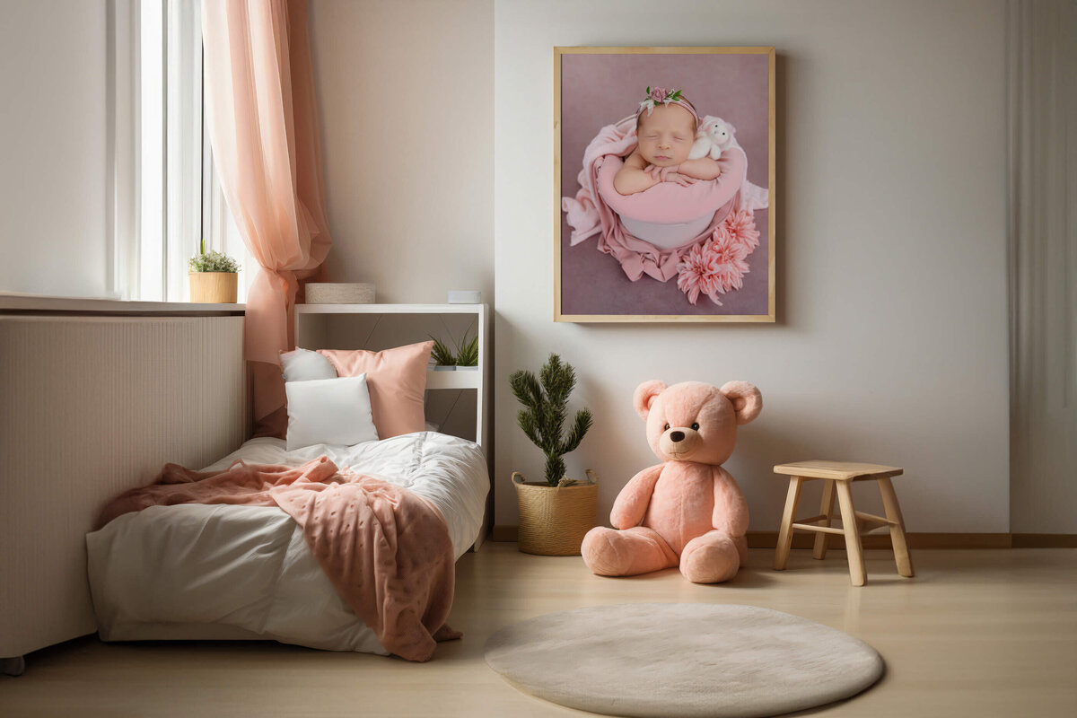 room with a framed photo on the wall with a newborn baby girl in a pink bucket for her Burlington, Ontario newborn photography session