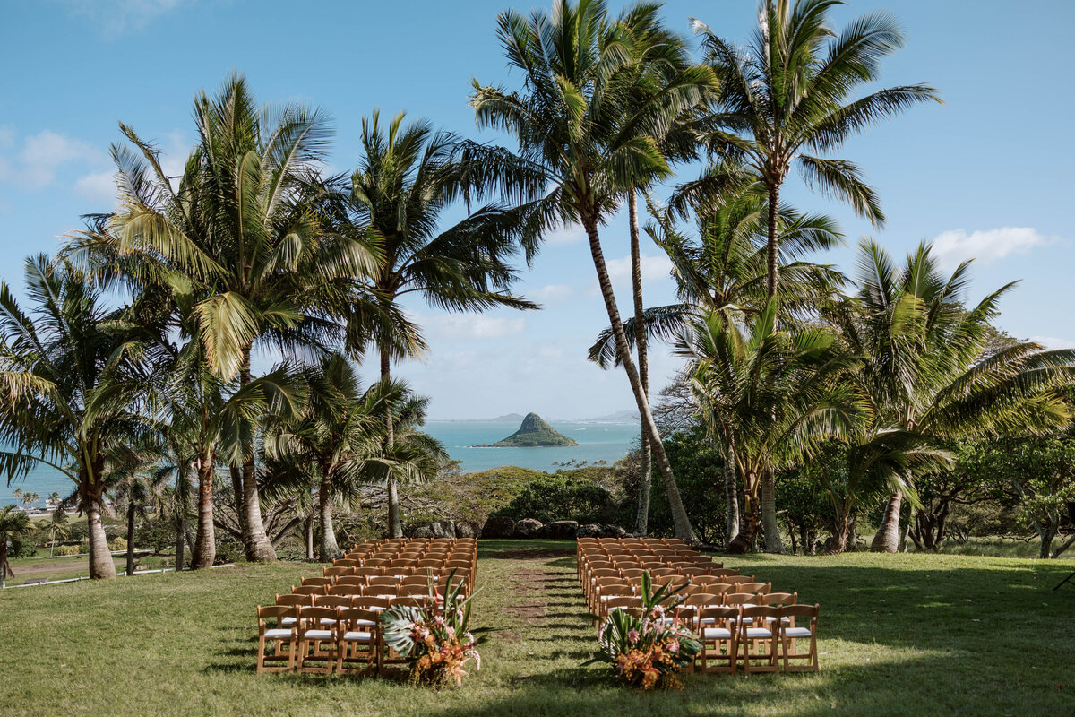 Stunning landscape shot overlooking Chinaman’s Hat from Paliku Gardens, with a ceremony setup and palm trees in perfect order, captured on film — by Kate Winters Photography.