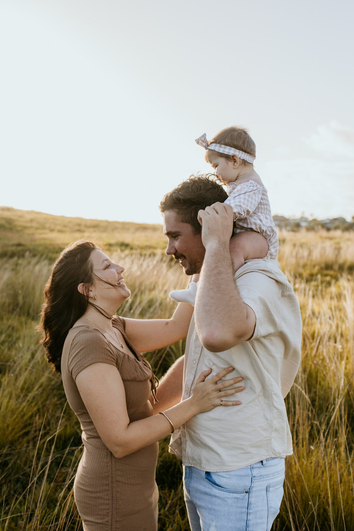 A candid moment of a baby on her dad’s shoulders, with mom playfully getting her attention.