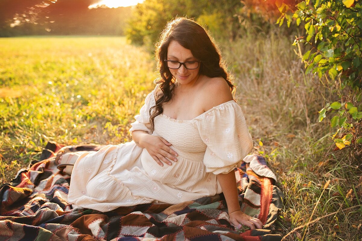 pregnant-woman-in-cream-dress-sitting-on-blanket-in-sunlit-field-during-golden-hour-maternity-session-in-indianapolis