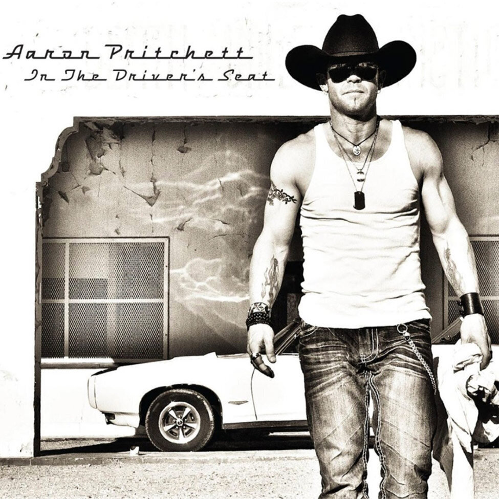 Album Cover Title In The Drivers Seat Country Music Artist Aaron Pritchett walking toward camera wearing tank top blue jeans cowboy hat convertible GTO in background behind him black and white