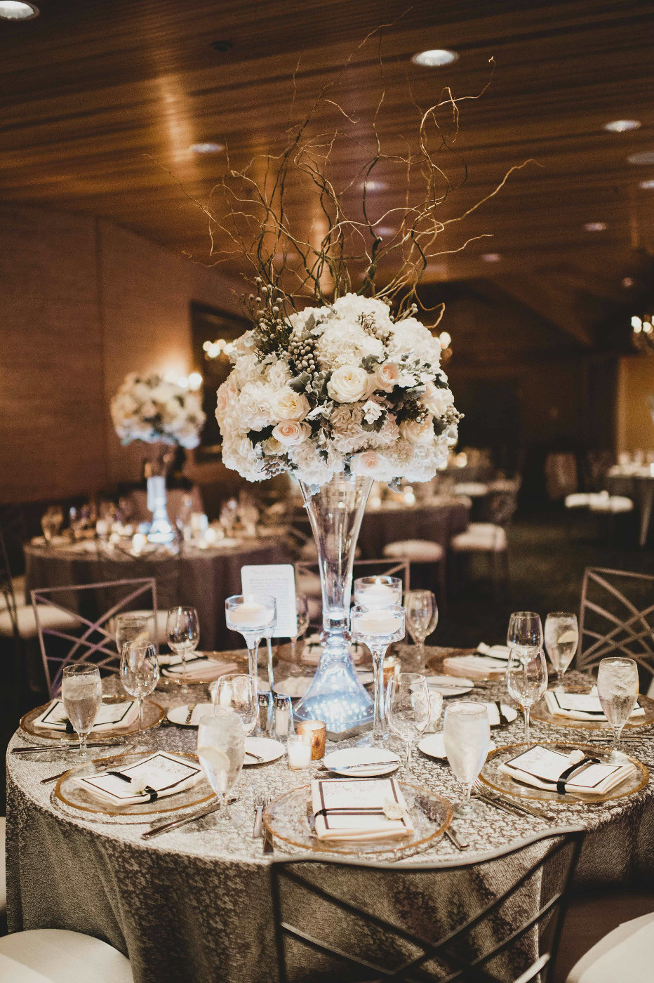 Luxurious tall table arrangement of willow, white hydrangea and eucalyptus with shimmery silver linens.